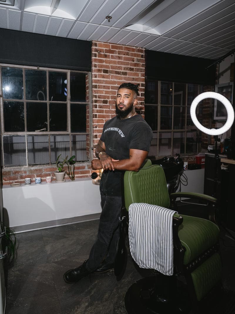 Barber Clipper Cole Knoll standing next to a green chair in a Charlotte, NC barbershop studio