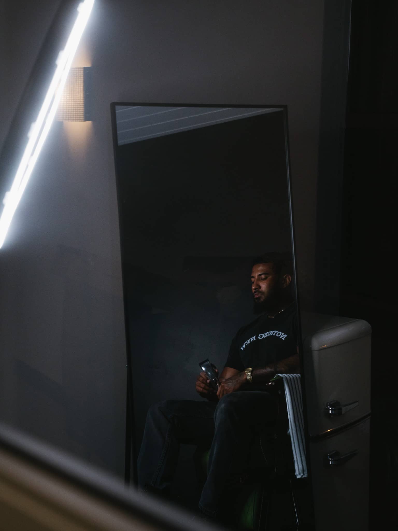 Clipper Cole Barber in Charlotte NC sitting in modern studio chair holding clippers, reflected in a mirror