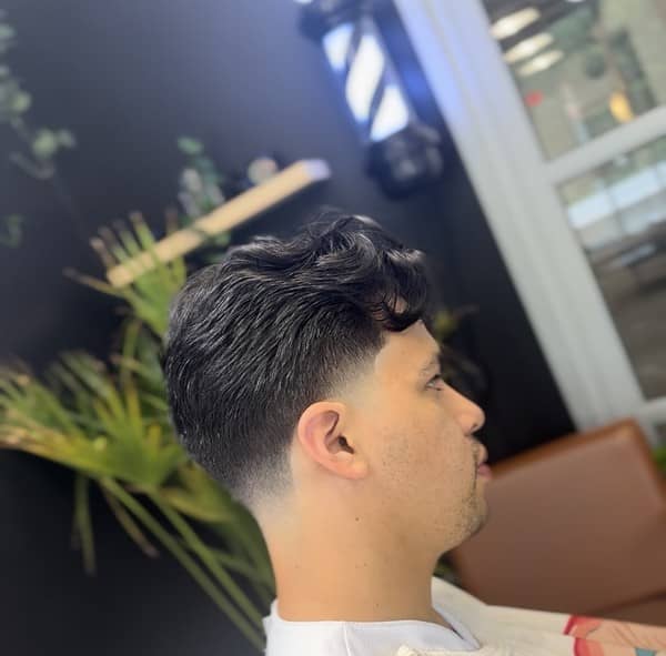 Side profile of a wavy textured hairstyle with mid fade, cut by Clipper Cole barber in Charlotte, NC